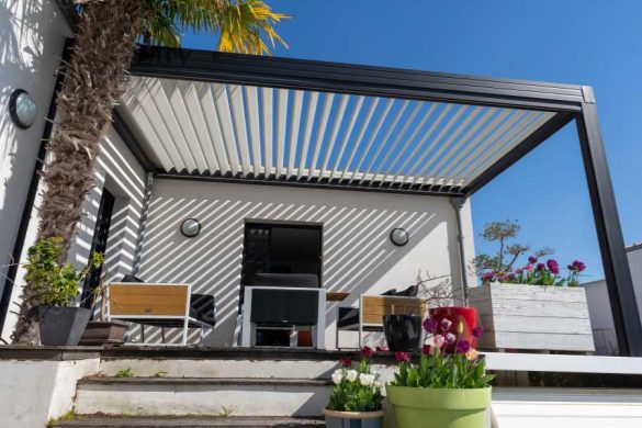 Véranda en aluminium noir avec lames orientables blanches sur terrasse fleurie par journée ensoleillée