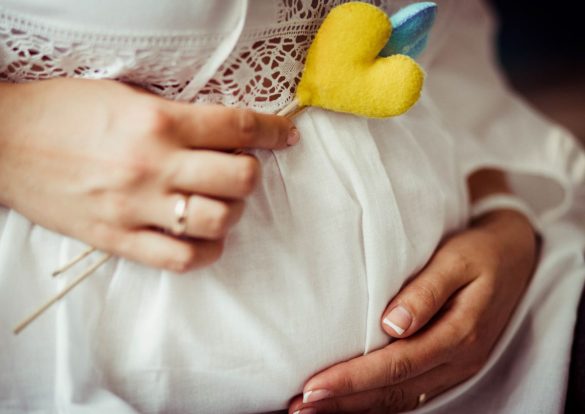 Gros plan sur le ventre rond d'une femme enceinte, tenant un cœur jaune et bleu, évoquant la douceur d'une Bola de Grossesse.
