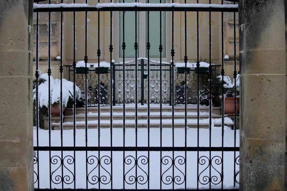 Portail maison en fer forgé recouvert de neige, ouvrant sur l’entrée d’une maison ancienne.