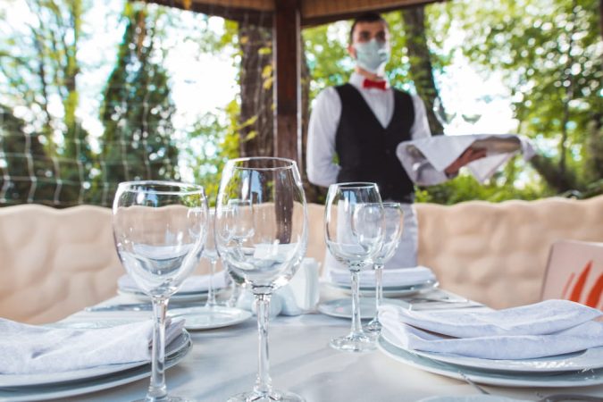 Serveur en tenue professionnelle dressant une table en extérieur, votre partenaire culinaire pour un service irréprochable