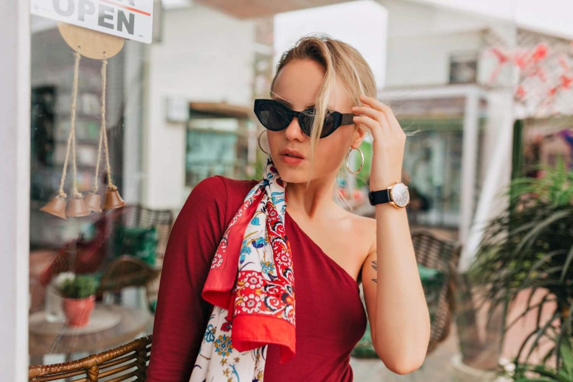 Jeune femme élégante portant des lunettes noires et un foulard coloré, illustrant la tendance accessoires été créateur soleil.